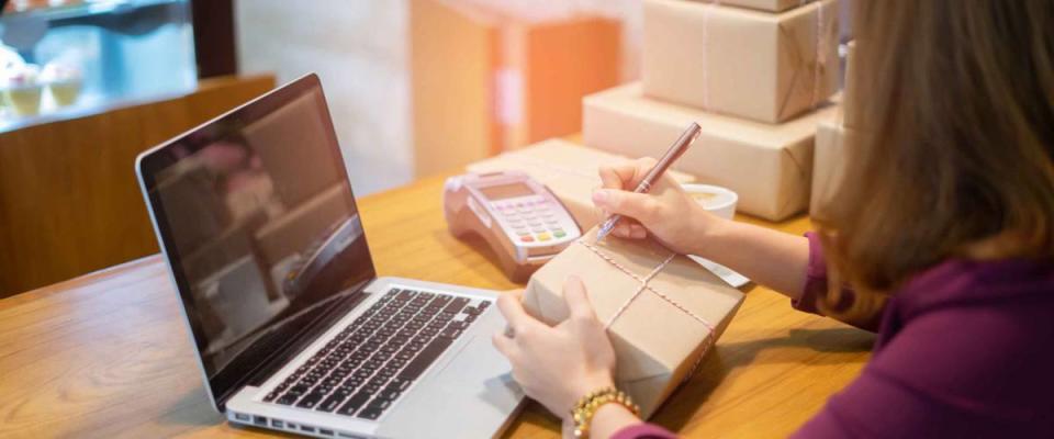 Young woman writing on box with laptop open in front of her