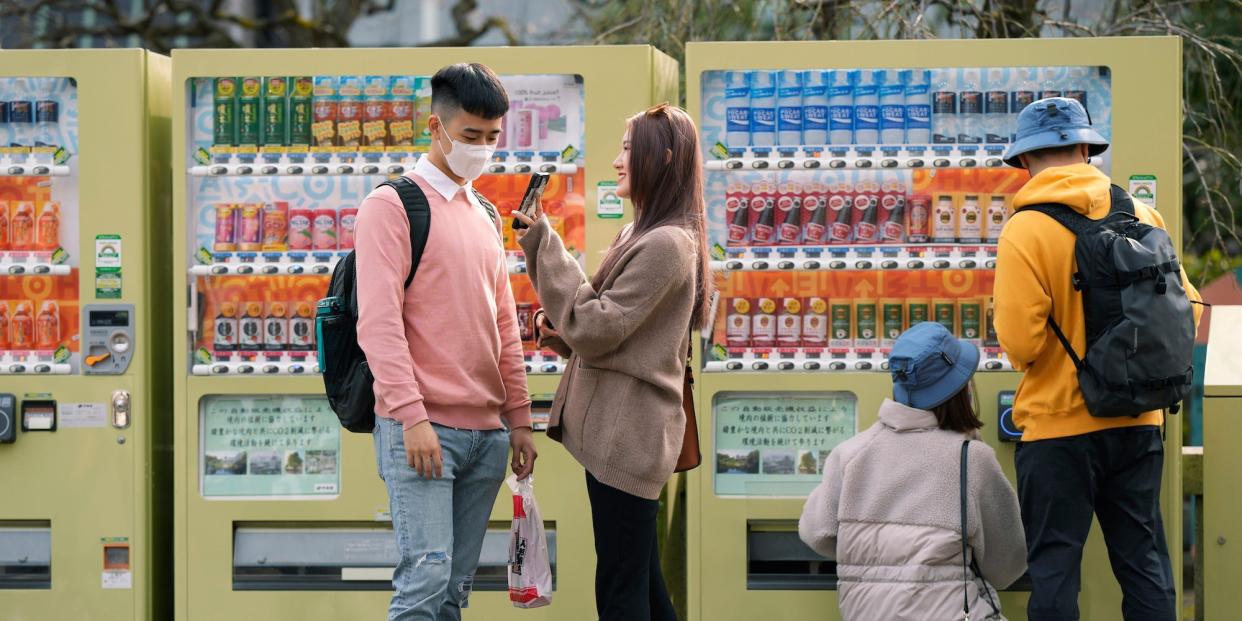 Tourists stand in front of a row of yellow vending machines in Tokyo, Japan, February 2023.