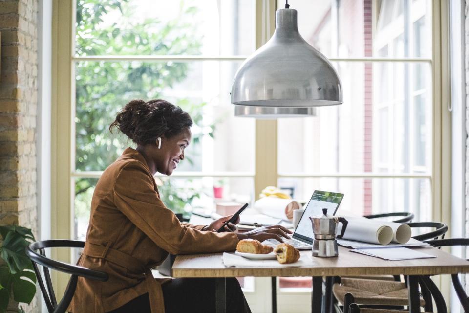 Smiling female architect using phone and computer while sitting at home office