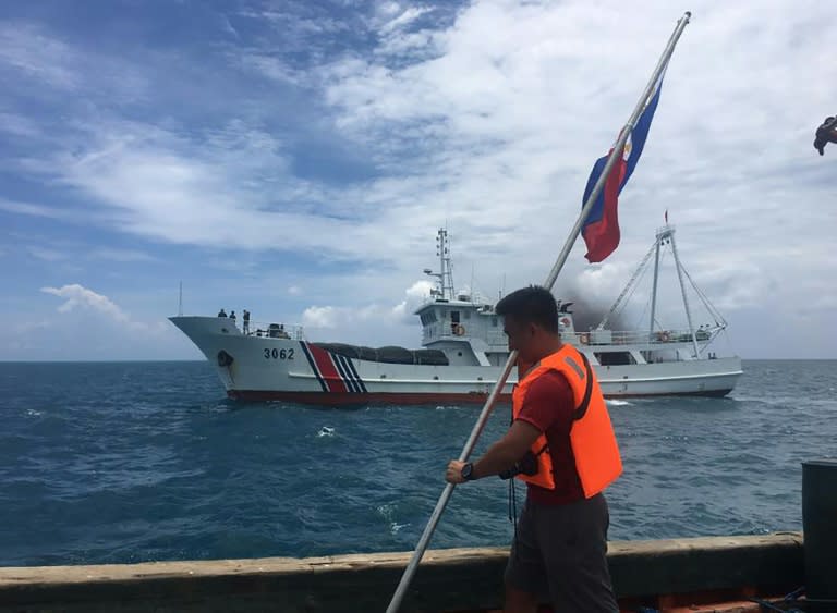 A Filipino activist holds a Philippine flag on a ship while a Chinese coast guard ship sails by at the Scarborough Shoal in the South China Sea