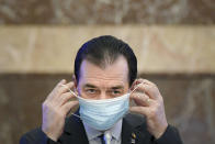 FILE - In this May 14, 2020 file picture Romanian Prime Minister Ludovic Orban handles his face mask before attending a meeting ahead of the loosening of measures taken by the government to combat the spread of the COVID-19 in Bucharest, Romania. Orban has paid fines totalling about dollars 600, Saturday, May 30, 20202, for smoking indoors and holding a meeting in his office where he and other participants, including several Cabinet ministers, did not wear face masks or follow social distancing rules imposed because of the COVID-19 coronavirus pandemic. (AP Photo/Andreea Alexandru, File)