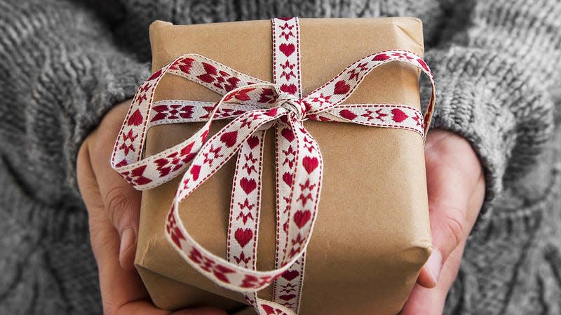 A child's hands are seen holding a present wrapped in brown paper and a ribbon.