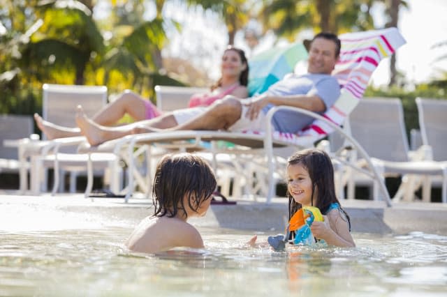 Siblings playing in pool at resort while parents sit in  background