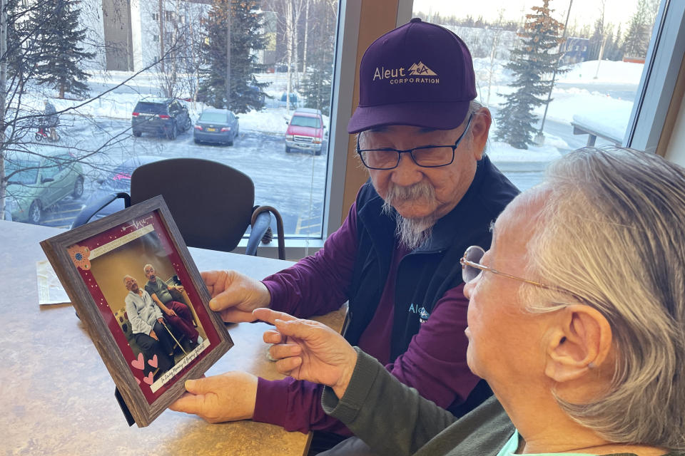 George Kudrin, left, and Pauline Golodoff hold a photo of Pauline and her late husband, Gregory Golodoff, Friday, Dec. 1, 2023, in Anchorage, Alaska. Gregory and his sister Elizabeth Golodoff Kudrin, George's late wife, were the last two living residents of Attu, Alaska, whose entire population was captured by the Japanese during World War II and sent to Japan until being liberated after the war. The community of Attu was not rebuilt, and residents were resettled elsewhere, mostly in Atka, Alaska. (AP Photo/Mark Thiessen)