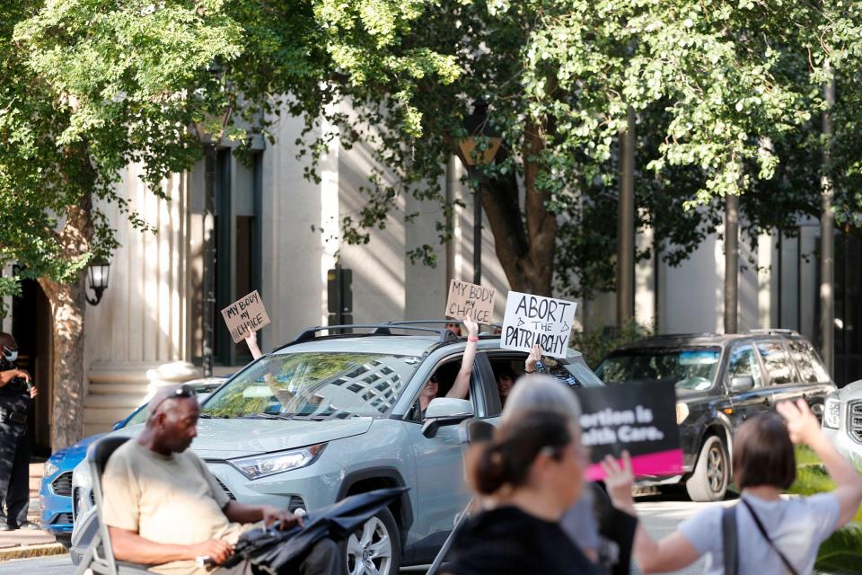 Passengers wave signs from their car and honk as they circle Johnson Square during Friday's abortion rights rally.