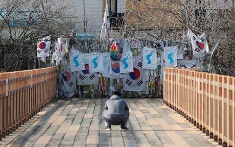 A man takes photographs near the wire fence decorated with national flags, unification flags and ribbons carrying messages wishing for reunification of the two Koreas at the Imjingak Pavilion in Paju - Credit: AP