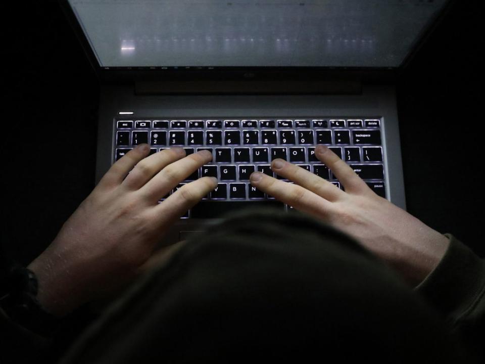 Person with a hoody typing at a computer in the dark. Suspicious online behavior