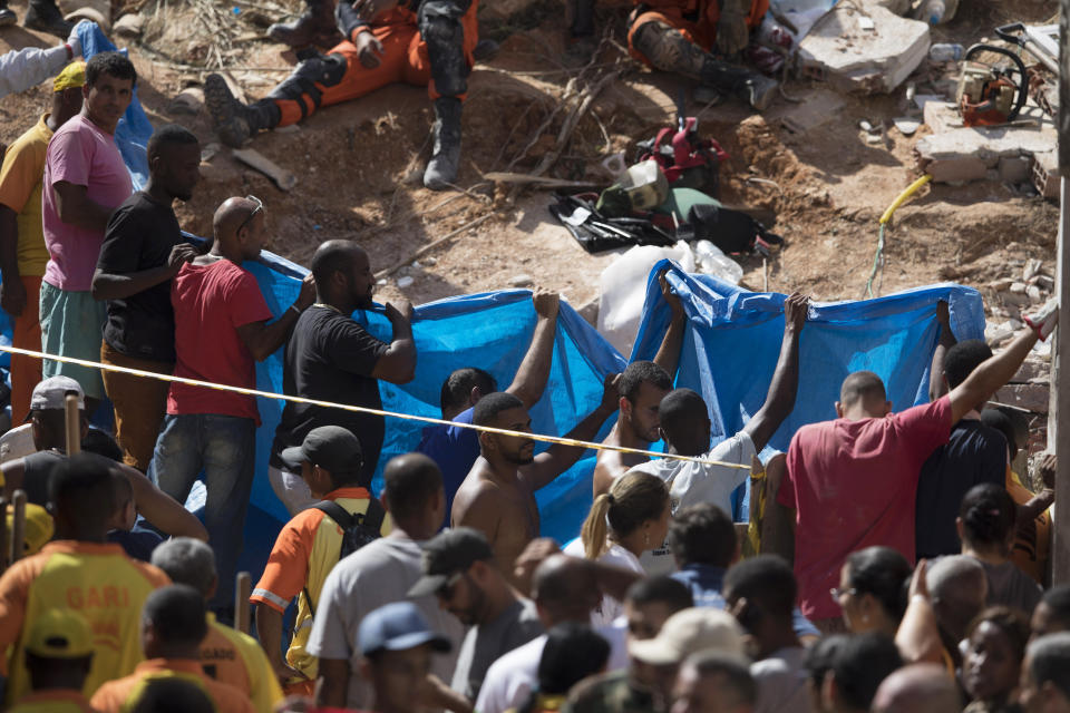 People holds up a sheet as firefighters work on the debris after a mudslide in Boa Esperanca or "Good Hope" shantytown in Niteroi, Brazil, Saturday, Nov. 10, 2018. Several people were killed and others injured in a mudslide near Rio de Janeiro on Saturday, Brazilian authorities said. (AP Photo/Leo Correa)