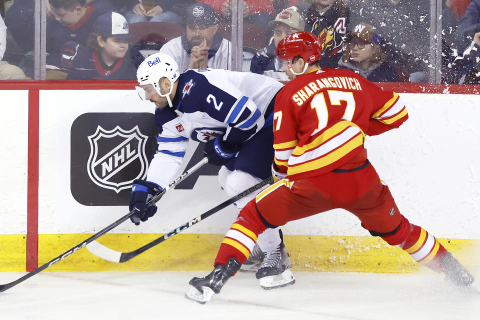 Winnipeg Jets' Dylan DeMelo (2) is checked by Calgary Flames' Yegor Sharangovich during the second period of an NHL hockey game in Calgary, Alberta, Monday, Feb. 19, 2024. (Larry MacDougal/The Canadian Press via AP)