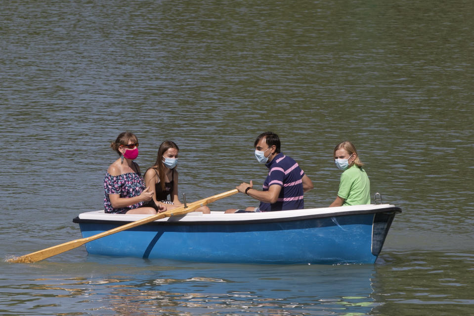 People wearing protective masks row a pleasure boat in the Retiro park, Madrid, Spain, Sunday, Aug. 23, 2020. Spain's top pandemic expert, Fernando Simon, has warned this week that "things are not going well" regarding the increase of infections that the country is seeing. (AP Photo/Paul White)