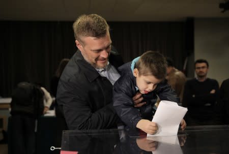 Adrian Zandberg holds a child who casts a ballot during parliamentary election at a polling station in Warsaw