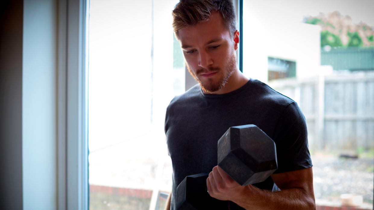  Man performs biceps curl with a dumbbell at home. 