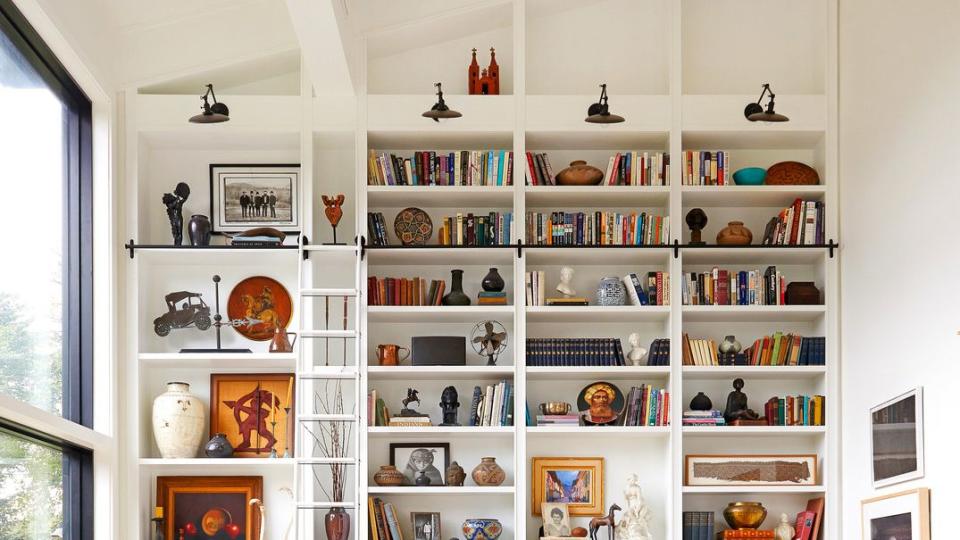 living room with high built in shelves, built ins, bookcase, white walls, ladder, storage, library