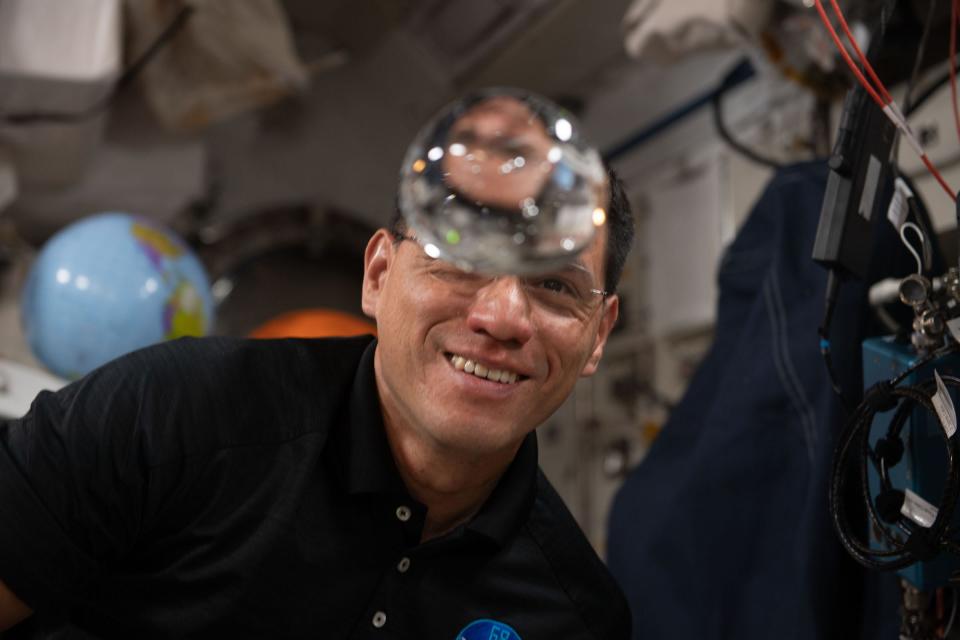 astronaut looks at floating bubble of water on international space station