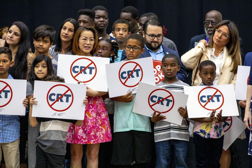 Kids holding signs against critical race theory stand on stage near Florida Gov. Ron DeSantis as he addresses the crowd before publicly signing HB7, dubbed the "Stop WOKE" bill by critics, during a news conference at Mater Academy Charter Middle/High School in Hialeah Gardens, Fla., on Friday, April 22, 2022.