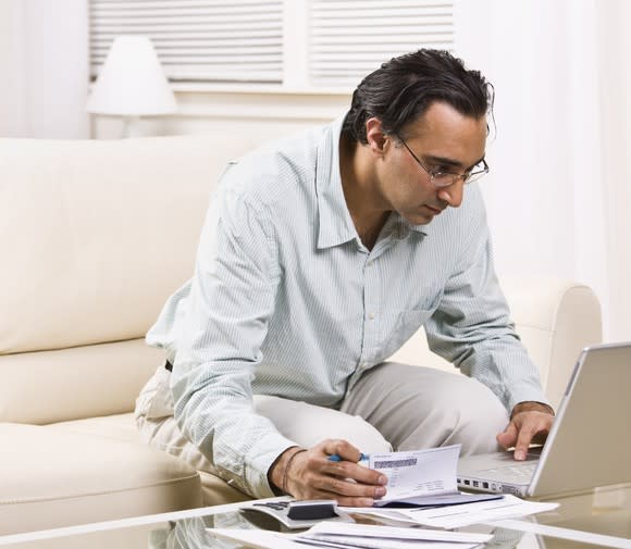 Man holding checkbook and looking at computer screen.