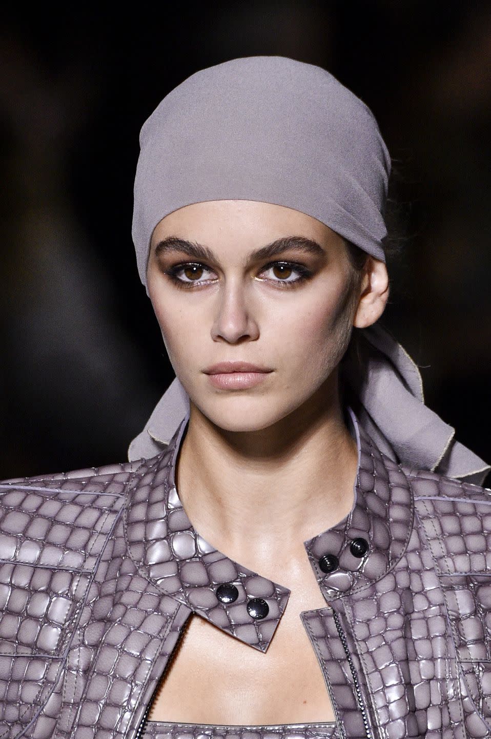 <p>Model Kaia Gerber walks the runway at Tom Ford wearing a silky, '70s-inspired headscarf tied around a not-too-messy bun crafted by hairstylist Orlando Pita.</p>