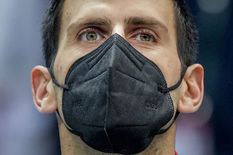 En esta foto del 26 de noviembre de 2021, el serbio Novak Djokovic usa una mascarilla durante la ceremonia de los himnos nacionales, antes de un partido de la Copa Davis entre su país y Austria, en Innsbruck. (AP Foto/Michael Probst)