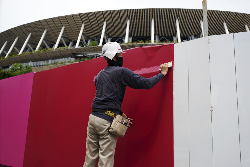 Workers place the overlay on the wall of the National Stadium, where opening ceremony and many other events are scheduled for the postponed Tokyo 2020 Olympics, Wednesday, June 2, 2021, in Tokyo. (AP Photo/Eugene Hoshiko)