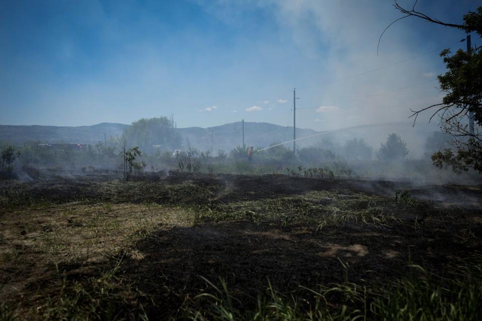 Un bombero dirige el agua sobre un incendio de pasto en un terreno detrás de una propiedad residencial en Kamloops, Columbia Británica (AP)