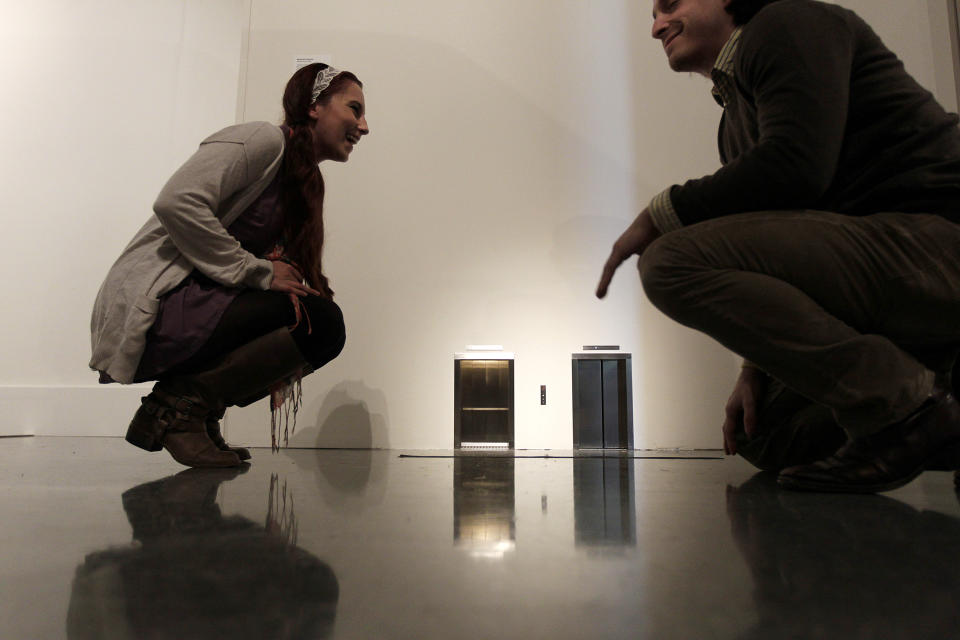 In this Wednesday, Nov. 14, 2012 photo, museum patrons react to the 2001 untitled mixed media piece by Maurizio Cattelan, tiny elevator doors that open and close, at the New Orleans Museum of Art. in New Orleans. The piece is is part of “Lifelike,” a traveling exhibit at the New Orleans Museum of Art through Jan. 27. (AP Photo/Gerald Herbert)