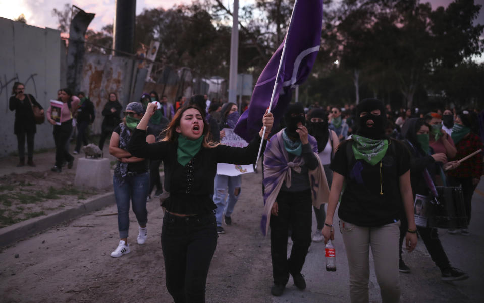 Women march against gender violence, one carrying a flag featuring the color historically associated with the push for gender equality, in Tijuana, Mexico, Friday, Feb. 21, 2020. When the body of law student Marbella Valdez was found at a garbage dump in Tijuana, the man who was obsessed with her demanded police solve the case, attended her funeral and a week later on Feb. 21 was arrested and charged with her murder. The man, identified by Mexican rules only by his first name, Juan, has insisted on his innocence. (AP Photo/Emilio Espejel)