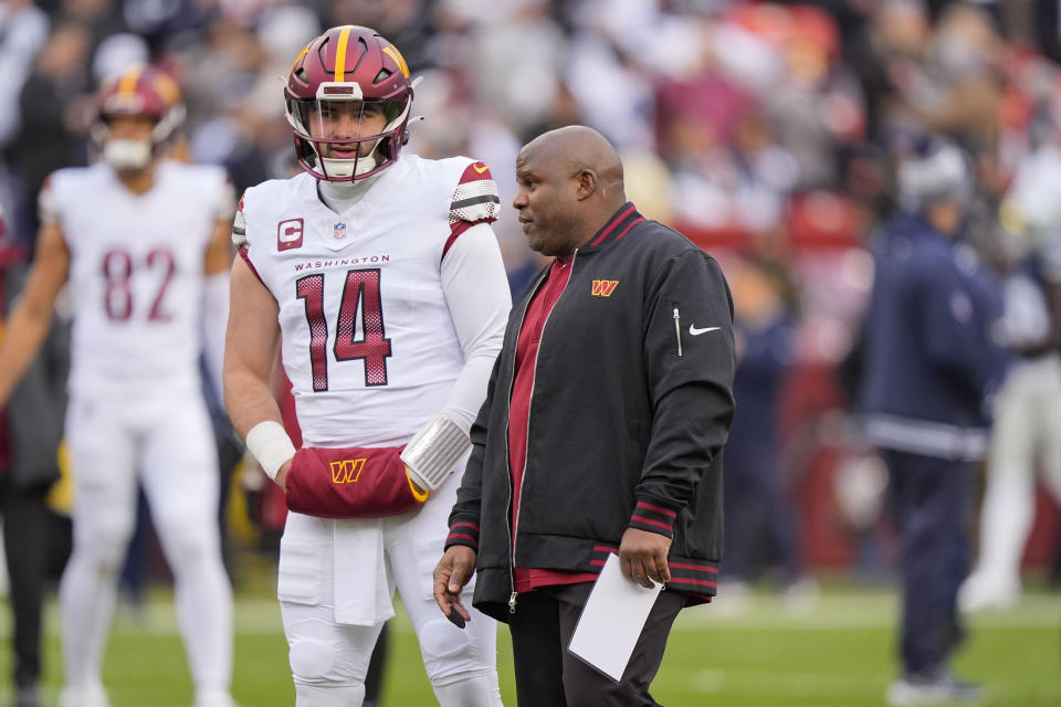 Washington Commanders quarterback Sam Howell (14) talking to Washington Commanders coach Eric Bieniemy, right, during pregame warmups before the start of the first half of an NFL football game, Sunday, Jan. 7, 2024, in Landover, Md. (AP Photo/Mark Schiefelbein)