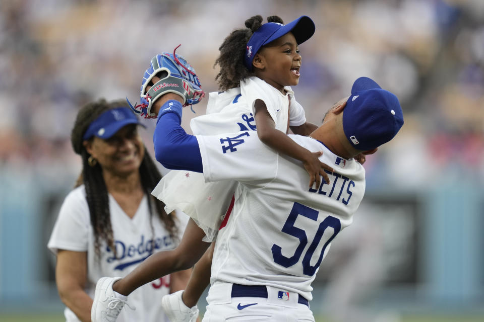 Kynlee Betts, center, greets her father, Los Angeles Dodgers right fielder Mookie Betts (50), after she threw out the first pitch with her grandmother, Diana Benedict, left, before a baseball game against the Minnesota Twins in Los Angeles, Monday, May 15, 2023. (AP Photo/Ashley Landis)