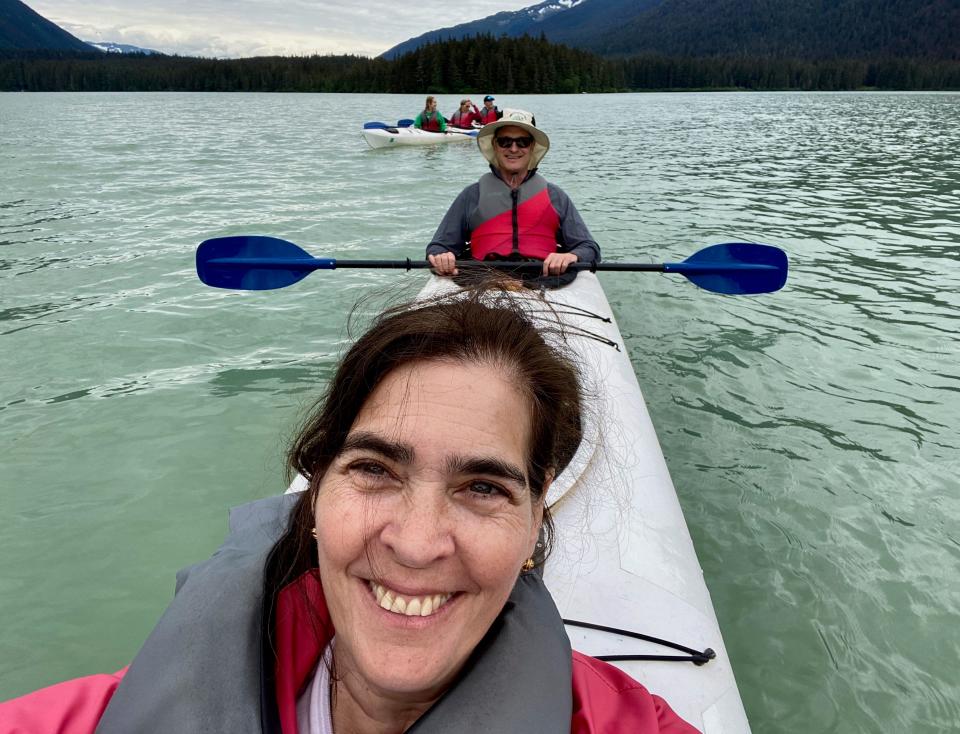 A woman takes a selfie on a kayak with a man onboard behind her.