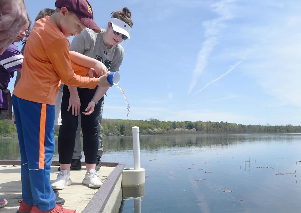 Earle C. Davis Primary School second-grader Jayin Best, 8, releases a small rainbow trout into Lake Pleasant with help from two friends, background, and Jenna Kunst, logistics coordinator for the North East School District STEM & Vine program.