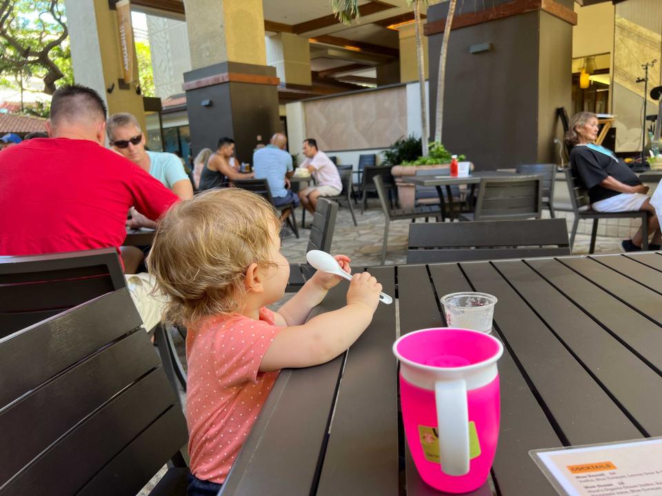 A child sitting at a table playing with a spoon with a water cup.