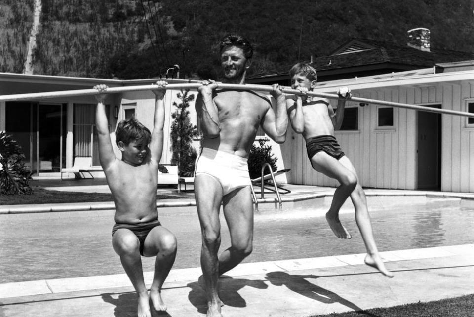 <p>Kirk Douglas uses a pole to lift his sons on the deck of a swimming pool, circa 1955. </p>