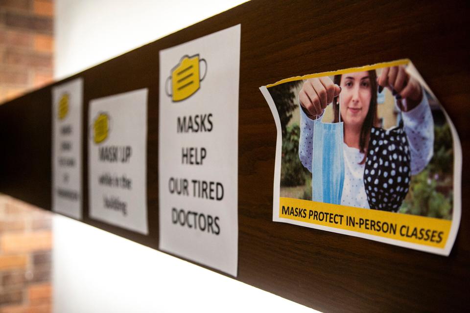 A piece of paper hanging in a staircase with a photo shows a person holding face masks with a caption "Mask protect in-person classes" is seen, Friday, Sept. 24, 2021, at the English Philosophy Building on the University of Iowa campus in Iowa City, Iowa.
