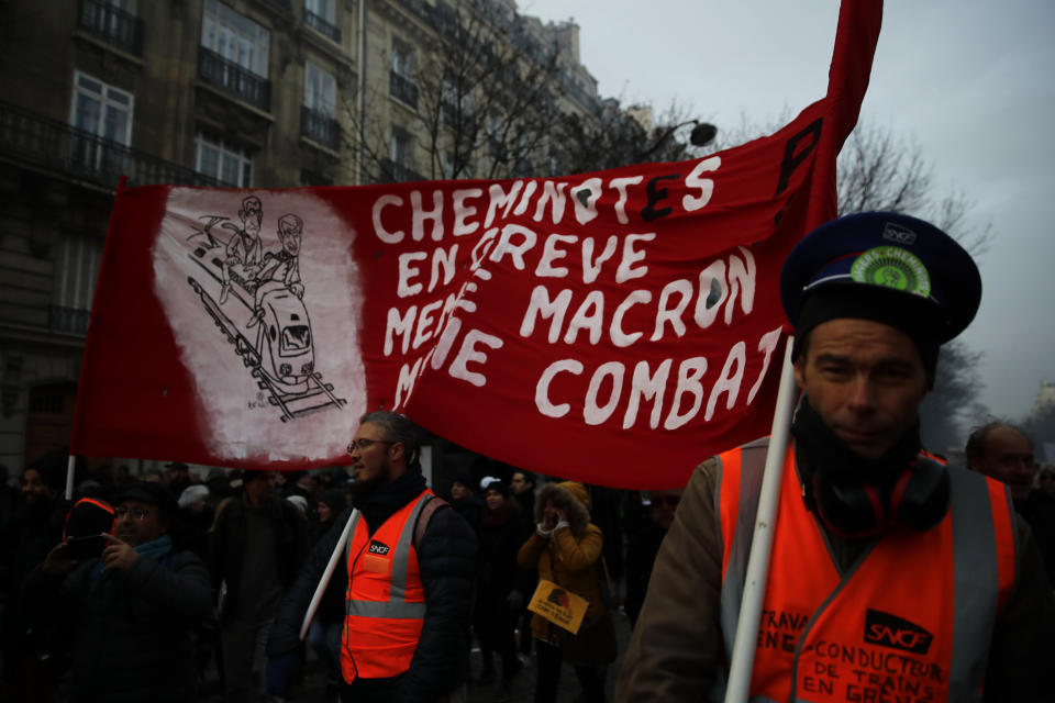 Rail workers hold a banner reading "Rail workers on strike, same Macron, same fight" during a demonstration Tuesday, Dec. 10, 2019 in Paris. French airport employees, teachers and other workers joined nationwide strikes Tuesday as unions cranked up pressure on the government to scrap upcoming changes to the country's national retirement system. (AP Photo/Christophe Ena)