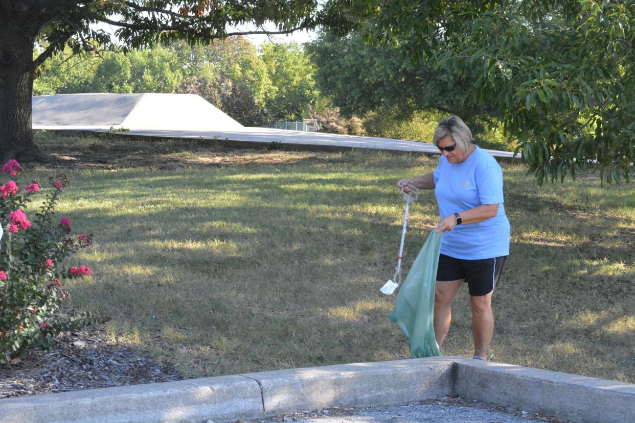 Jackie Reed with the Columbia South Rotary Club picks up trash Saturday near the skate park in Cosmo Park as part of a collaborative effort of the city's service clubs for a park cleanup.