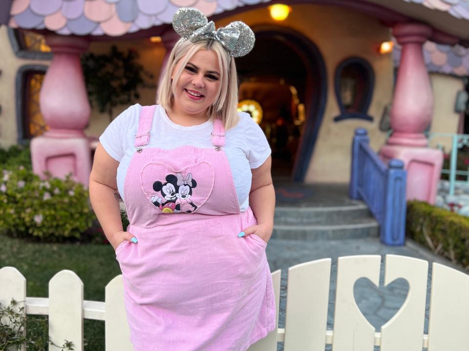 dana posing in front of minnies house at disneyland wearing a pink coverall