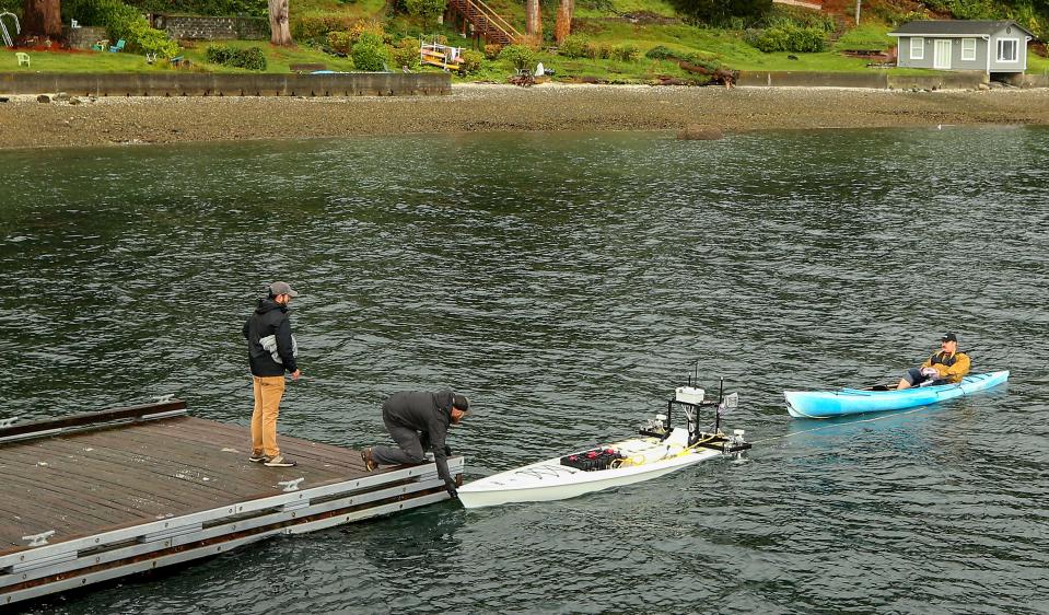 Serco senior systems engineer Michael Yount, middle, helps guide the ARCHER Environmental unmanned surface vehicle towing Troy Barnhart behind it in a kayak, to the dock, at the Port of Illahee Pier on Wednesday, Oct. 25, 2023.