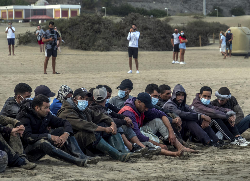 Migrants from Morocco sit on a beach after arriving at the coast of the Canary Island, crossing the Atlantic Ocean sailing on a wooden boat on Tuesday, Oct.20, 2020. Some 1,000 migrants have spent the night again sleeping in emergency tents in a dock while authorities in the Canary Islands complain that the Spanish government keeps blocking transfers of newly arrived migrants to the mainland over coronavirus concerns. (AP Photo/Javier Bauluz)