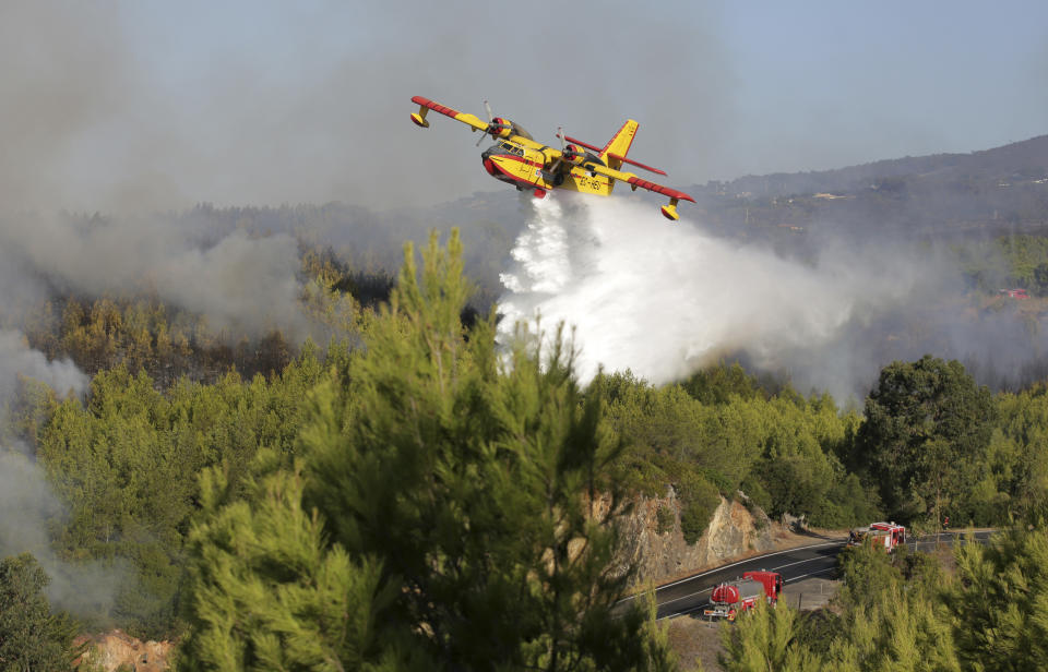 A firefighting airplane drops its load next to firetrucks on a road outside the village of Charneca, in the Sintra national park, west of Lisbon, Sunday, Oct. 7, 2018. Over 700 firefighters were battling a forest fire that started overnight about 40 kilometers (25 miles) west of Lisbon. (AP Photo/Armando Franca)