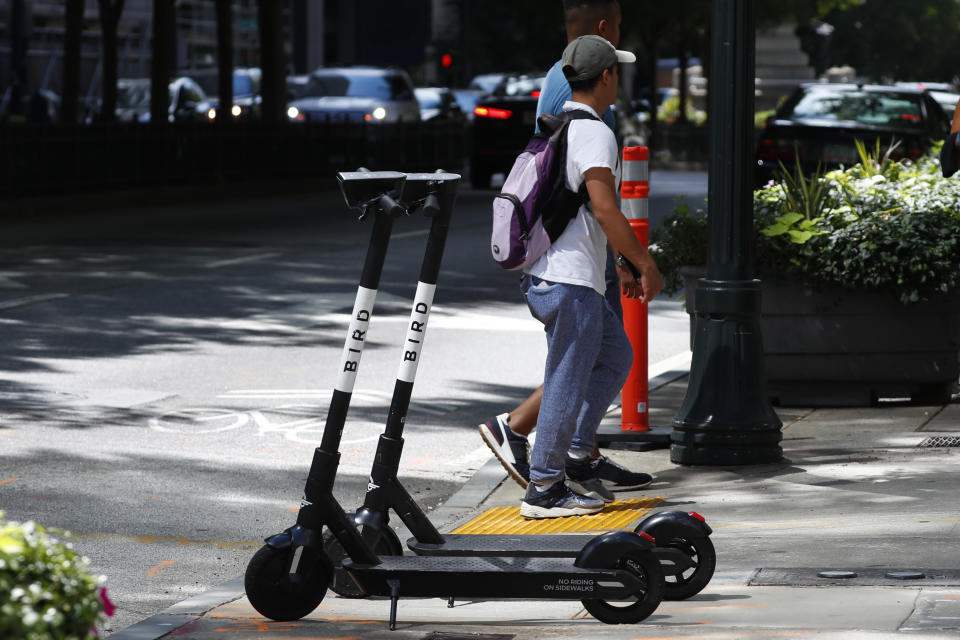 Pedestrians walk past a electric scooters Thursday, Aug. 8, 2019, in Atlanta. Atlanta is banning electric scooters during nighttime hours during a deadly summer for riders. The ban comes as cities across the nation struggle to regulate the companies renting the devices and keep riders safe. In Atlanta, three riders have died since May in Atlanta crashes that involved a public bus, an SUV and a car. Police in the Atlanta suburb of East Point say a fourth rider was killed there Tuesday in a collision involving his scooter and a truck. (AP Photo/John Bazemore)