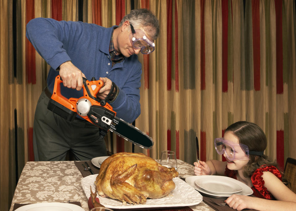 Girl (8-9) watching father cutting turkey using chainsaw at dining room table