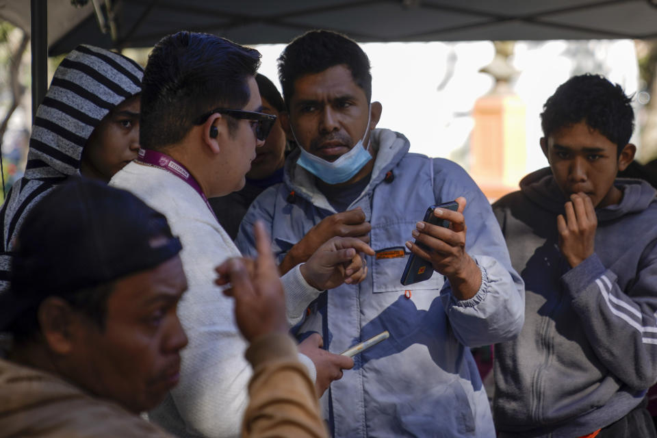 FILE- Migrants get help with the CBPOne app from a Tijuana, Mexico city worker Tuesday, Jan. 24, 2023, in Tijuana, Mexico. Asylum-seekers say joy over the end of the public health restriction known as Title 42 this month is turning into anguish with the realization of how the Biden administration's new rules affect them. Though the government opened some new avenues for immigration, many people's fate is largely left up to a U.S. government app that is limited and unable to decipher and prioritize human suffering and personal risk. (AP Photo/Gregory Bull)