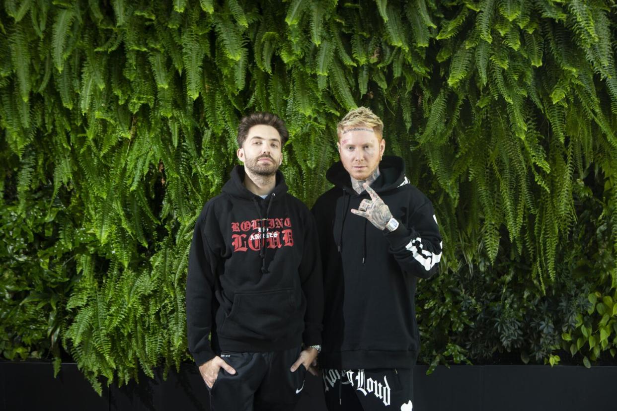 Two men standing next to each other in front of a grass wall