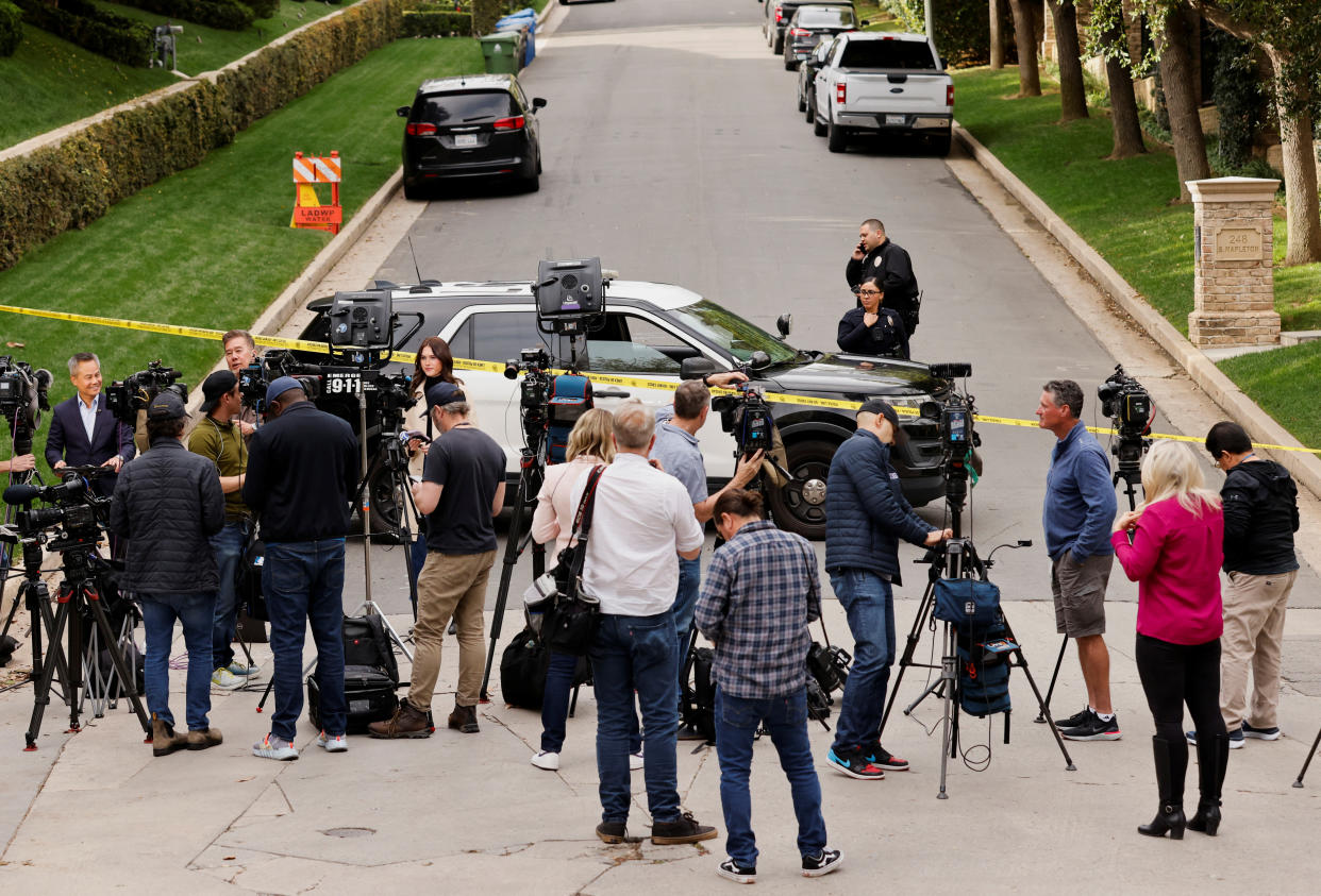 About a dozen media members in the middle of the street work as two law enforcement officers stand behind police tape outside Combs’s L.A. property.