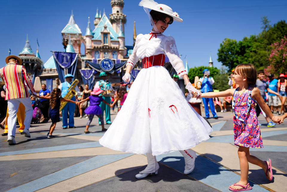 Mary Poppins wearing a white dress and hat, holding hands with a child in a colorful dress at Disneyland