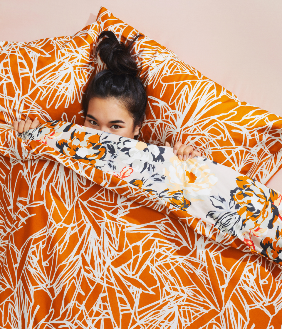 Girl with dark hair tied up on her head lies in a bright orange and white bed set including doona cover and pillows. It reverses to a floral pattern.