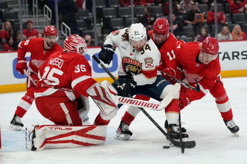 Red Wings defenseman Simon Edvinsson (3), right wing Filip Zadina (11) and Panthers defenseman Casey Fitzgerald reach for the puck in from of goaltender Ville Husso during the first period on Monday, March 20, 2023, at Little Caesars Arena.