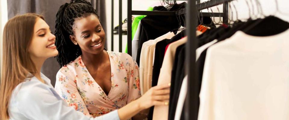 Two woman smiling, browsing clothing racks