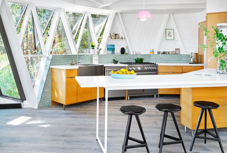 airy kitchen with island with black stools and orangey wood cabinetry