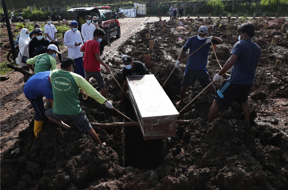 Workers lower a coffin into a grave during a burial at the special section of Jombang Public Cemetery reserved for those who died of COVID-19, in Tangerang on the outskirts of Jakarta, Indonesia, Monday, June 21, 2021. Indonesia saw significant spikes in confirmed COVID-19 cases recently, an increase blamed on travel during last month's Eid al-Fitr holiday as well as the arrival of new virus variants, such as the the Delta version first found in India. (AP Photo/Tatan Syuflana)